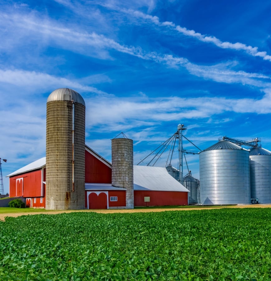 Red barn with silos and grain bins next to lush green field under blue sky