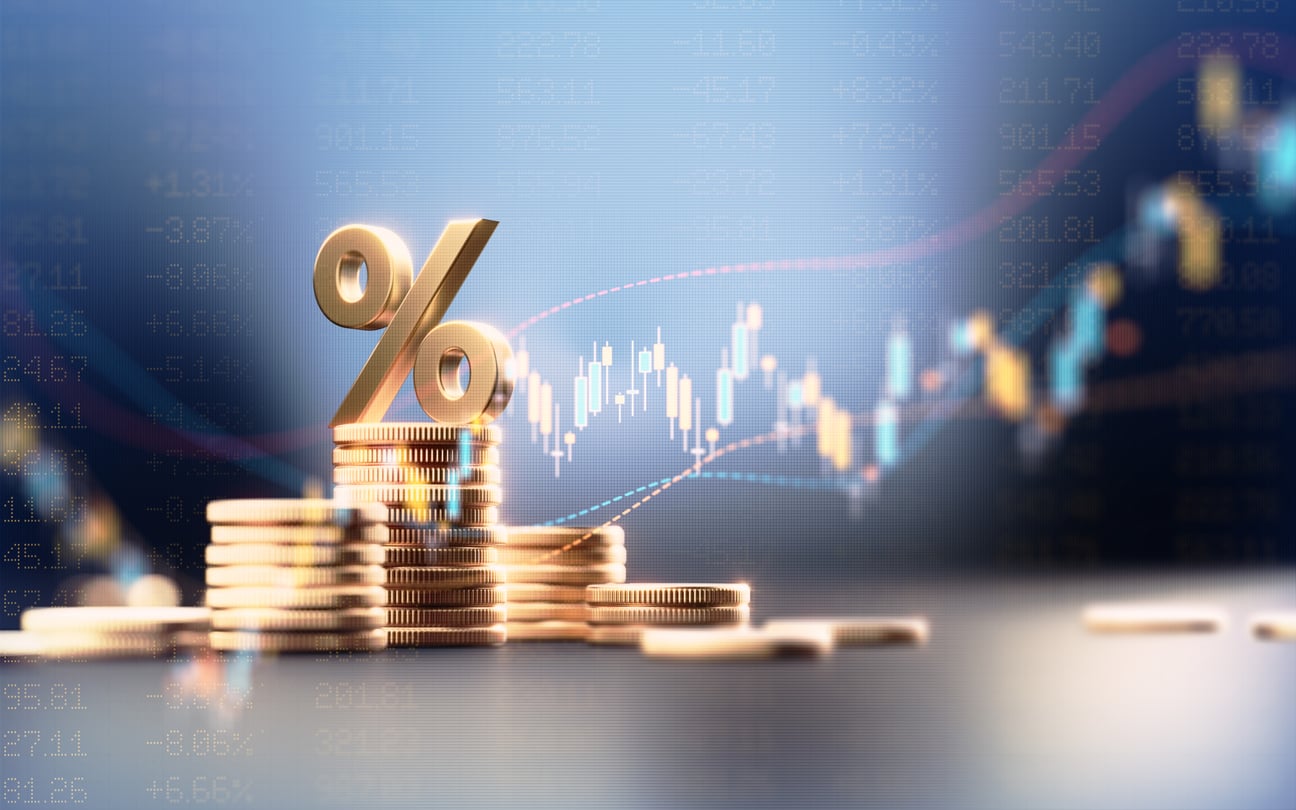 Golden percentage symbol atop stacked coins with financial stock market graph in background.